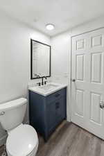 Half bath featuring a textured ceiling, vanity, and dark wood finished floors
