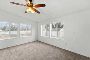 Carpeted empty room featuring ceiling fan and vaulted ceiling