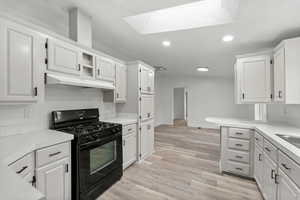 Kitchen featuring black gas range, light countertops, white cabinets, recessed lighting, and open shelves