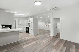 Kitchen with light countertops, gas stove, white cabinets, cooling unit, and light wood-style flooring