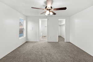 Unfurnished bedroom with light colored carpet, a walk in closet, connected bathroom, and a ceiling fan