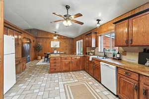 Kitchen with a peninsula, lofted ceiling, white appliances, brown cabinetry, and wooden walls
