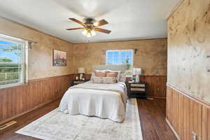Bedroom featuring wainscoting, wood walls, a ceiling fan, ornamental molding, and dark wood-style floors