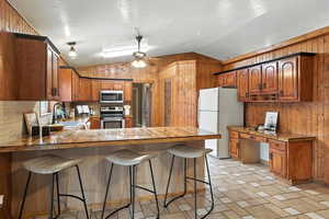 Kitchen featuring a peninsula, lofted ceiling, stainless steel appliances, brown cabinets, and a breakfast bar area