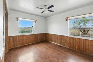 Empty room featuring wooden walls, dark wood finished floors, a wainscoted wall, crown molding, and ceiling fan