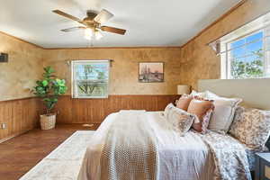 Bedroom with wood finished floors, wooden walls, wainscoting, a ceiling fan, and ornamental molding