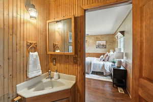 Ensuite bathroom featuring wood walls, vanity, and dark wood-type flooring