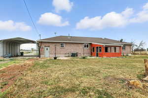 Back of house featuring a lawn, a detached carport, and brick siding