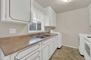 Kitchen with white cabinetry, washing machine and clothes dryer, white electric range oven, and light countertops
