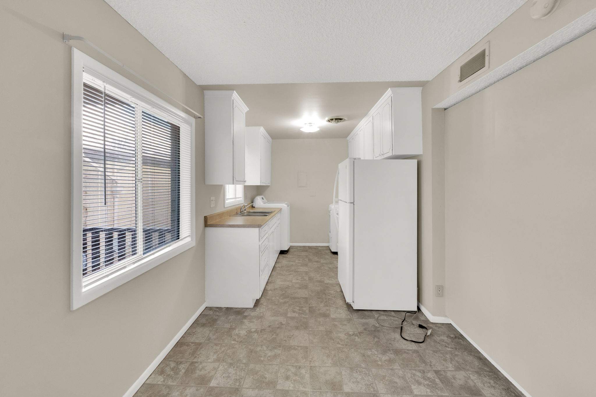 Kitchen featuring freestanding refrigerator, white cabinets, light countertops, a textured ceiling, and washer / dryer