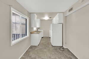 Kitchen featuring freestanding refrigerator, white cabinets, light countertops, a textured ceiling, and washer / dryer