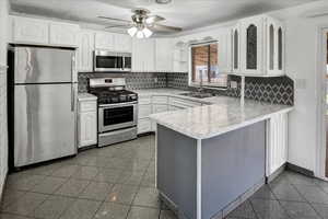 Kitchen featuring appliances with stainless steel finishes, light countertops, white cabinets, a peninsula, and a textured ceiling