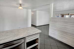 Kitchen featuring light countertops, white cabinetry, dishwasher, a textured ceiling, and granite floors