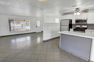Kitchen featuring stainless steel appliances, a textured ceiling, white cabinets, backsplash, and a ceiling fan
