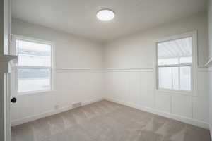 Empty room with a decorative wall, a wainscoted wall, light carpet, and plenty of natural light