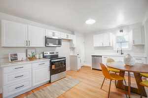 Kitchen with appliances with stainless steel finishes, white cabinets, and light wood-style floors