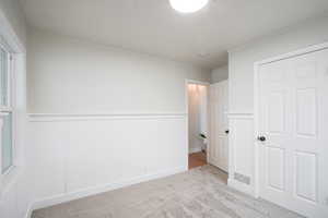 Unfurnished bedroom featuring a wainscoted wall, light colored carpet, and a decorative wall