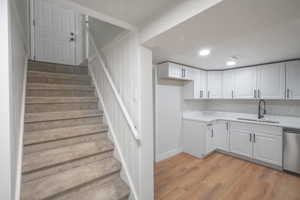 Kitchen with white cabinets, stainless steel dishwasher, light wood-type flooring, recessed lighting, and light stone countertops