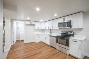 Kitchen with stainless steel appliances, white cabinets, light countertops, light wood-type flooring, and recessed lighting
