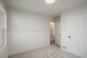 Unfurnished bedroom featuring a wainscoted wall, carpet floors, and a decorative wall