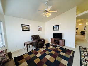 Living area featuring vaulted ceiling, a ceiling fan, a textured ceiling, and light colored carpet