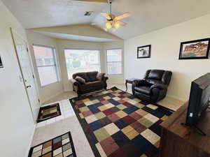 Living area with a textured ceiling, light carpet, lofted ceiling, ceiling fan, and light tile patterned floors