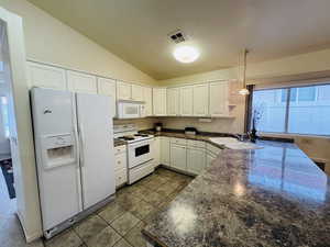 Kitchen featuring white appliances, plenty of natural light, hanging light fixtures, vaulted ceiling, and white cabinets