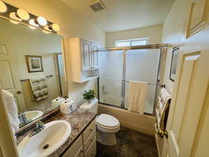 Bathroom featuring vanity, combined bath / shower with glass door, and a textured ceiling
