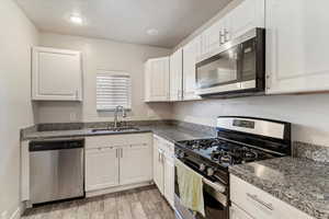 Kitchen with stainless steel appliances, white cabinetry, dark stone counters, a textured ceiling, and wood tiled floors