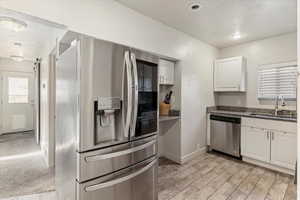 Kitchen with stainless steel appliances, white cabinetry, a textured ceiling, dark stone countertops, and wood finish floors