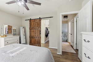 Primary Bedroom with dark wood-type flooring, a spacious closet, a ceiling fan, and a barn door