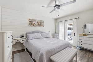 Primary Bedroom with wood walls, dark wood-type flooring, a ceiling fan, and access to exterior