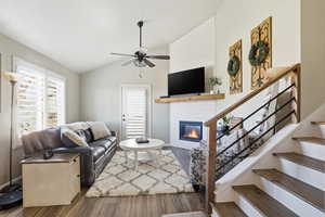 Living area featuring lofted ceiling, wood finished floors, a large fireplace, stairs, and ceiling fan
