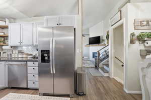 Kitchen with open shelves, cabinetry, stainless steel appliances, tasteful backsplash, and light wood-style floors