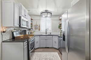 Kitchen with dark countertops, appliances with stainless steel finishes, open shelves, decorative backsplash, and light wood-style floors