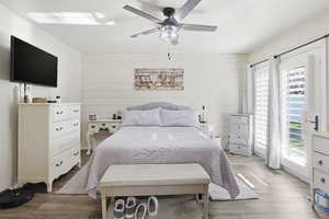 Primary Bedroom with access to exterior, ceiling fan, wood finished floors, and wooden walls