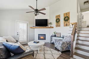 Living area featuring vaulted ceiling, stairway, dark wood-style floors, and a glass covered fireplace