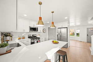 Kitchen with a breakfast bar, appliances with stainless steel finishes, white cabinetry, recessed lighting, and a peninsula
