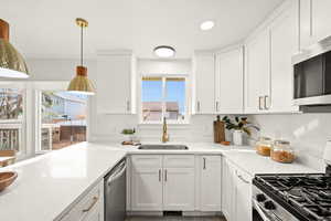 Kitchen featuring appliances with stainless steel finishes, white cabinets, decorative light fixtures, recessed lighting, and light stone countertops