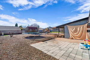 Fenced backyard with a trampoline, a playground, and a patio area