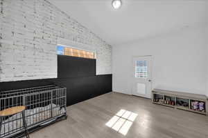 Bedroom featuring brick wall, multiple windows, lofted ceiling, and light wood finished floors