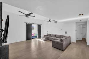 Living area featuring a barn door, ceiling fan, light wood-style floors, and a wall mounted air conditioner
