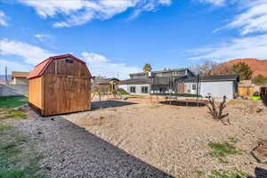 Back of house with a storage unit, a trampoline, a playground, and a fenced backyard