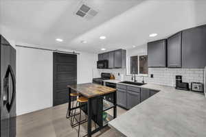 Kitchen with a barn door, black appliances, gray cabinets, decorative backsplash, and light wood-type flooring