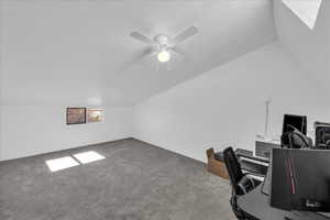 Carpeted office space with vaulted ceiling, a skylight, a textured ceiling, and ceiling fan