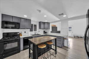 Kitchen featuring black appliances, a kitchen breakfast bar, tasteful backsplash, wood counters, and gray cabinetry