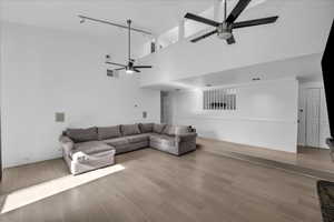 Living room with light wood-type flooring, a wainscoted wall, ceiling fan, and a high ceiling