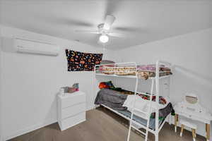 Bedroom featuring a wall unit AC, light wood-type flooring, and a ceiling fan
