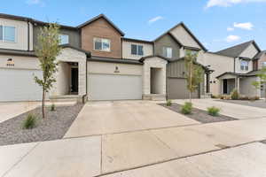 View of front facade with stone siding, driveway, stucco siding, and an attached garage