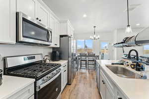 Kitchen with appliances with stainless steel finishes, hanging light fixtures, light stone counters, white cabinets, and light wood-type flooring